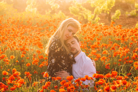 Man and woman with closed eyes embracing in poppy field on the dusk,  countryside Maltaの写真素材