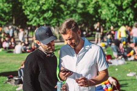 Helsinki, Finland - June 29, 2019: Two men with rainbow on cheeks looking in smartphone on Helsinki Pride festival in Kaivopuisto public parkのeditorial素材
