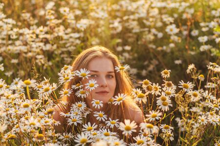 Portrait of pretty blond woman sitting in chamomile field in sunsetの写真素材