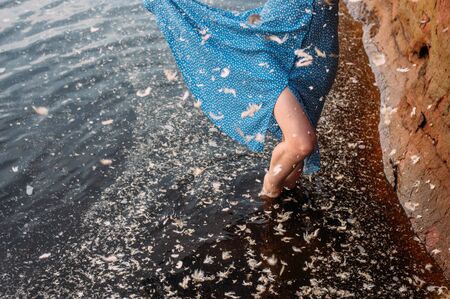 Girl staying in water near red sand wall in river, many feathers in water
