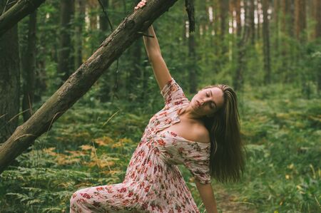 Portrait of young beautiful girl in summer dress in forest that holds tree trunkの写真素材