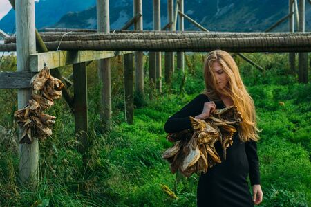 Girl in black dress with bundle of dried fish heads, Lofoten Islands, Norway