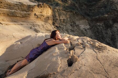 Brown-haired woman in purple glittering dress lies on sand slopeの写真素材
