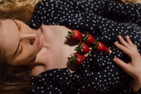Beautiful blond girl with closed eyes lies on earth with strawberry over her chestの写真素材