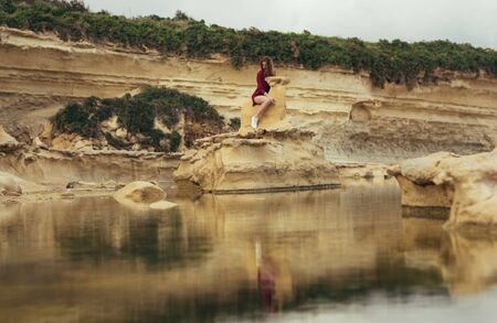 Beautiful blond smiling girl in purple dress sitting on stone on natureの写真素材