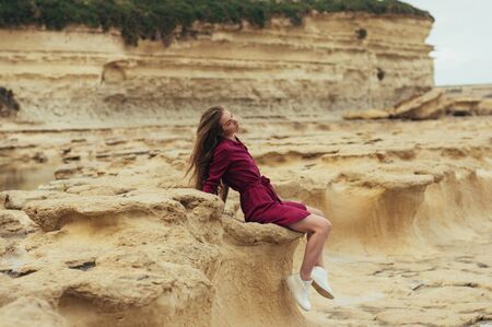 Beautiful blond girl in purple dress sitting on stone on natureの写真素材