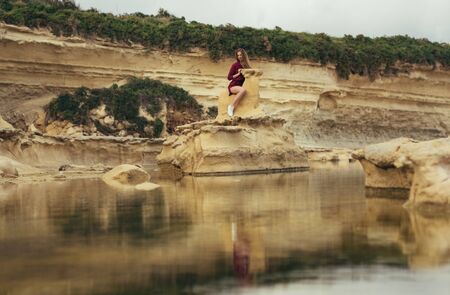 Beautiful blond smiling girl in purple dress sitting on stone on natureの写真素材
