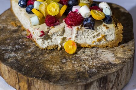 Fruit cheesecake with strawberry, blueberry, kumquat and cape gooseberry on the wooden old tree cutの写真素材