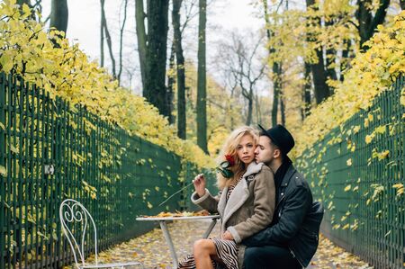 Couple siiting on chair at the center of passage and embracing, girl holds red rose in hand and looking to cameraの写真素材