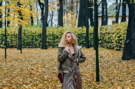 Young blond girl walking in public park in fall and looking to sideの写真素材