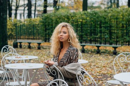 Young blond girl sitting at table in public park in fall and looking to cameraの写真素材