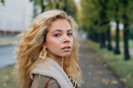 Young blond girl walking in public park in fall and looking to cameraの写真素材