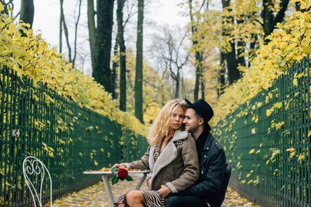 Couple siiting on chair at the center of passage and embracing, girl holds red rose in hand and looking to cameraの写真素材