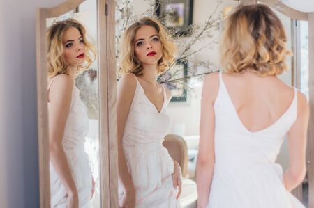 Beautiful blond girl with vintage make up and hairstyle staying near triple mirror and looking to the cameraの写真素材