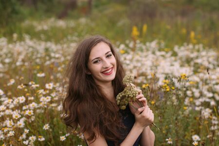 Young beautiful girl holds bouquet of flowers in hands in chamomile field in summerの写真素材