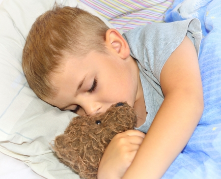 Beautiful little boy sleeping with his teddy bearの写真素材