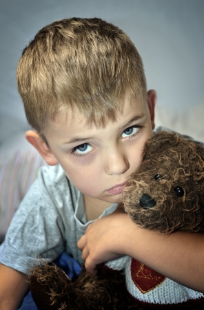 Sad little boy with a bruise under his eye clutching a teddy bear. Domestic violence.の写真素材