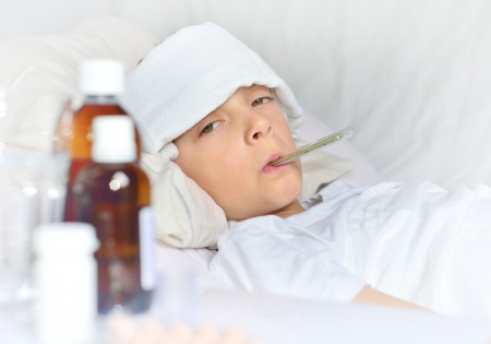 Sick boy lying in bed with a compress and thermometerの写真素材