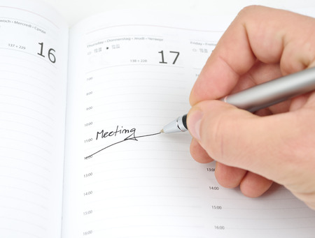 Hand with pen writes hour meeting in the calendar scheduleの写真素材