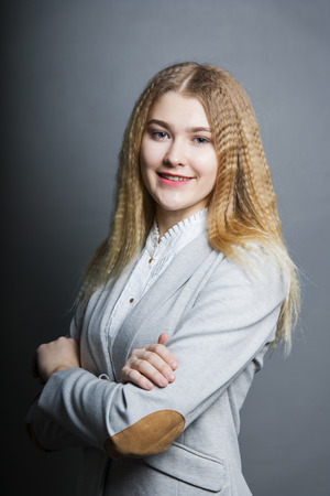 Young smiling business woman in an official suit standing on the gray backgound, arms crossedの写真素材