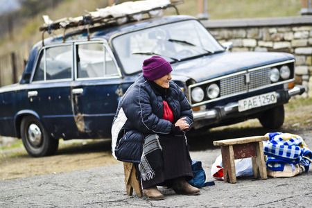 Mtskheta, Georgia, November 18, 2014: An old woman sitting in front of an old car in Mtskheta, Georgia, Europe.のeditorial素材