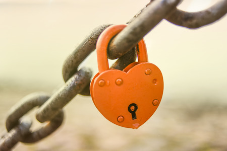 Padlock in a shape of heart locked on a chain.