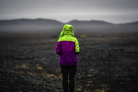 Woman looking on a Iceland landscape, black volcanic dust and mountains with fog in background.の写真素材
