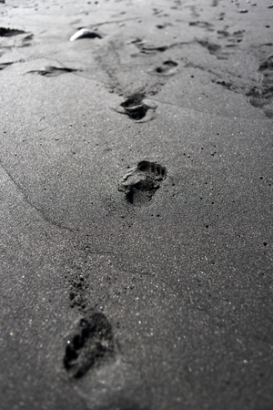 Footprints on the beach on black volcanic sand.の写真素材