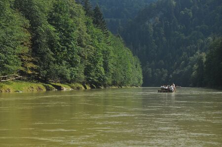 Rafting on the Dunajec River in the Pieniny National Park on wooden folding shuttles tied with a rope. Rafters paddling on a rapid stream with a rocky bottom and strong river current.の写真素材