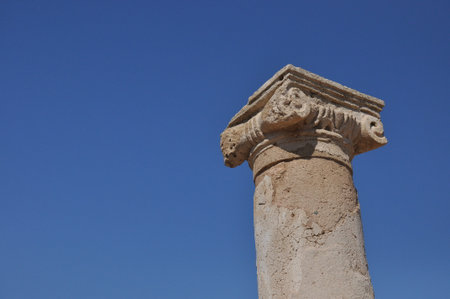 A weathered stone column stands tall, showing intricately carvings under a bright blue sky. This historical site offers a glimpse into ancient architecture and craftsmanship.の写真素材