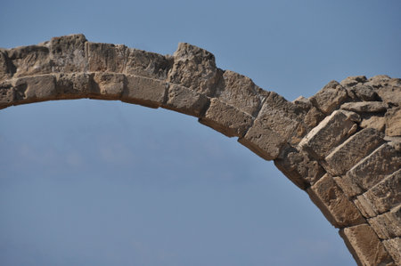 Fragments of a weathered stone arch stand against a bright blue sky, showing the remnants of ancient architecture and its storied past.の写真素材