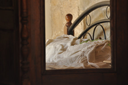 A warm and inviting bedroom features a neatly made bed with a soft blanket, seen through the reflection in a wooden mirror, creating a serene atmosphere.の写真素材