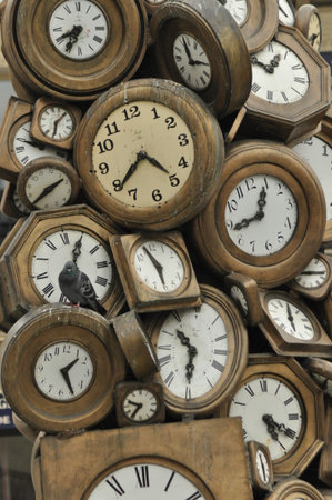 A collection of vintage clocks in various shapes and sizes is grouped together, each showing a different time. This display highlights beautiful craftsmanship and history.の写真素材
