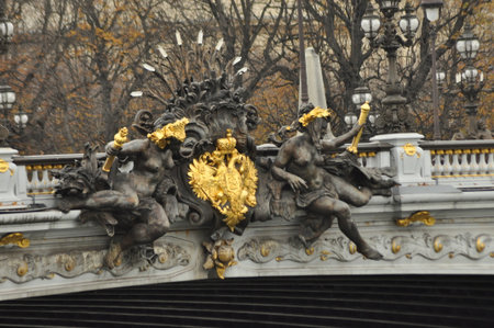 Intricate sculptures adorn an elegant bridge, showcasing golden details against a backdrop of autumn trees. The artwork captures historical themes and adds charm to the urban landscape.の写真素材