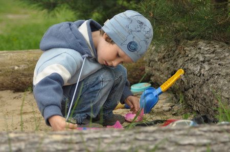 A young child is focused on playing with various colorful toys while seated near a log in a green outdoor area. Soft grass surrounds the scene, creating a peaceful atmosphere.の写真素材