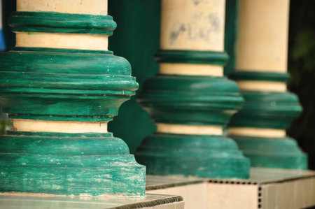 Three green pillars with intricate designs stand tall by a peaceful outdoor area. The setting conveys a sense of calm and history under clear blue skies.の写真素材