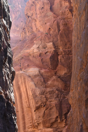 Hikers explore a narrow canyon surrounded by towering sandstone cliffs under bright sunlight. The vibrant reddish hues create a breathtaking landscape that attracts nature lovers.の写真素材