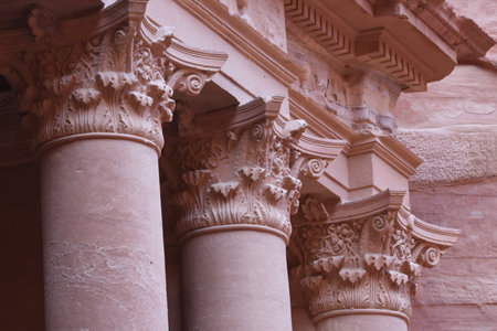 Ornate stone columns stand proudly in Petra, Jordan, reflecting the craftsmanship of ancient builders. The warm light of dust highlights the detailed carvings and historical significance.の写真素材