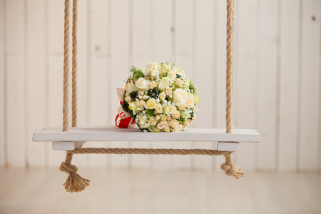 wedding rose bouquet of bride on wooden swing with ropeの写真素材