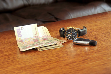 Men watch with a black leather wristband, ukraine money, car trinket on a wooden tableの写真素材