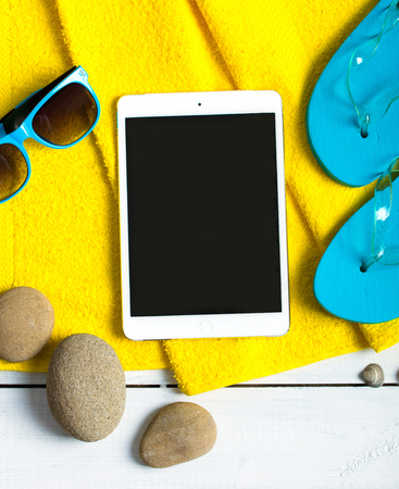 Summer concept of tablet pc, flip flop shoes, sunglasses on pier near hotel poolの写真素材