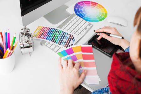 young woman artist in jeans jacket drawing something on graphic tablet at the officeの写真素材