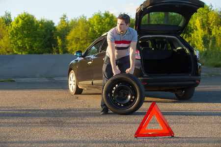 Photo of man holding spare wheel against broken carの写真素材