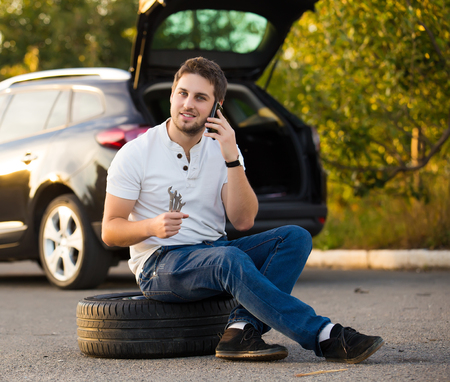 Sad and depressed man sitting near car with punctured tireの写真素材