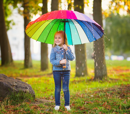 The image of a little girl with a rainbow umbrella in parkの写真素材
