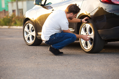 Sad and depressed man sitting near car with punctured tireの写真素材