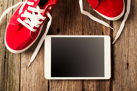 Concept with red sneakers and tablet on wooden floor background.の写真素材