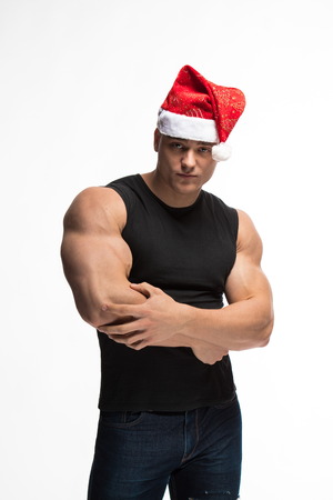 athlete bodybuilder posing with a cap of Santa Claus on a white backgroundの写真素材