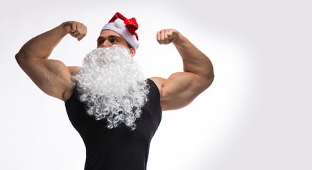 athlete bodybuilder posing with a beard and a cap of Santa Claus on a white backgroundの写真素材