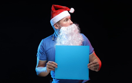 portrait actor male in cap and beard of Santa Claus with a sheet of paper for notes in the hands on a black backgroundの写真素材